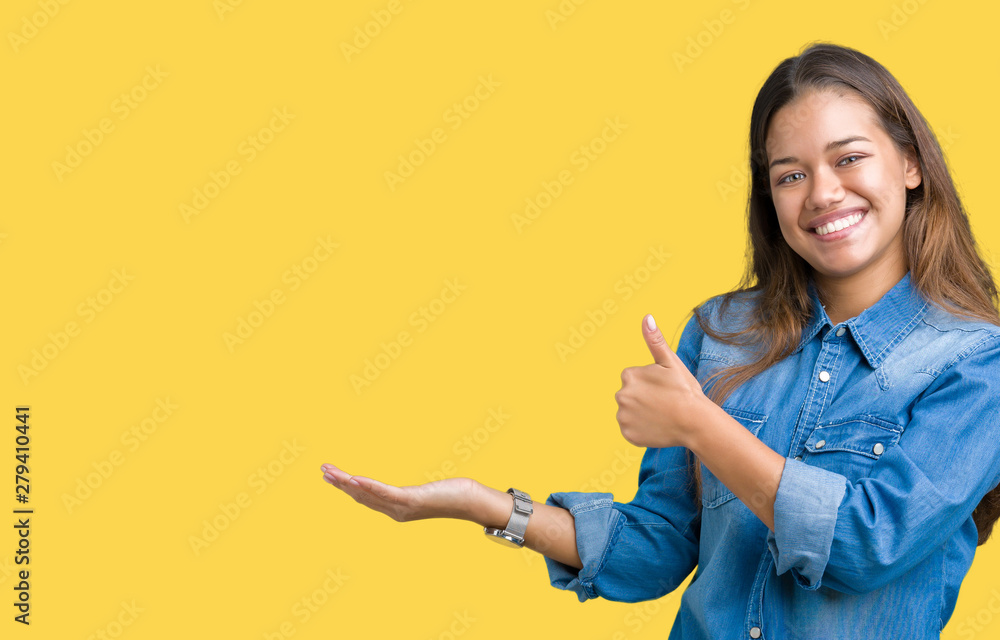 Young beautiful brunette woman wearing blue denim shirt over isolated background Showing palm hand and doing ok gesture with thumbs up, smiling happy and cheerful Young beautiful brunette woman wearing blue denim shirt over isolated background Showing palm hand and doing ok gesture with thumbs up, smiling happy and cheerful