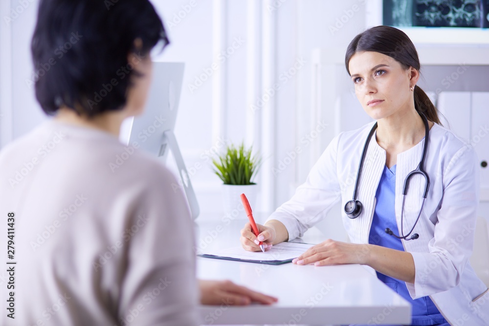 Doctor and patient discussing medical problems in a hospital consulting room. Doc filling in a patient's form Doctor and patient discussing medical problems in a hospital consulting room. Doc filling in a patient's form