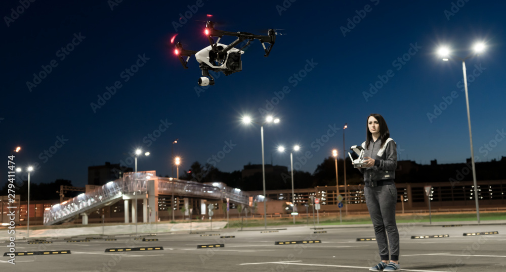 The girl controls the quadcopter. Drone in the night sky. The operator of the copter. The night sky and the lights. Flights on the quadrocopter. The girl controls the quadcopter. Drone in the night sky. The operator of the copter. The night sky and the lights. Flights on the quadrocopter.