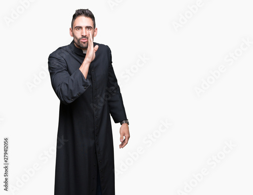 Young Christian priest over isolated background hand on mouth telling secret rumor, whispering malicious talk conversation