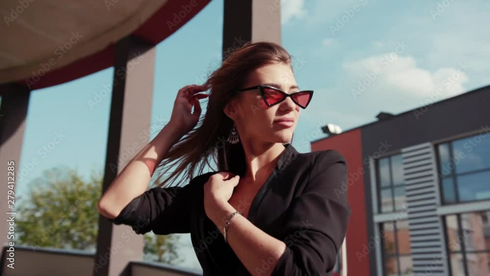 Beautiful gorgeous young woman in stylish suit stroking her hair in strong wind and playfully poses on camera outdoors. Fashionable trendy accessories. Confidence, female power concept Beautiful gorgeous young woman in stylish suit stroking her hair in strong wind and playfully poses on camera outdoors. Fashionable trendy accessories. Confidence, female power concept