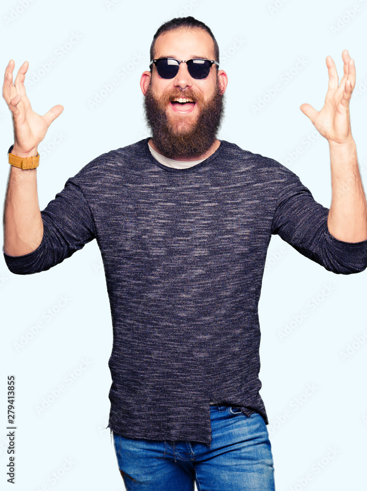 Young hipster man wearing sunglasses celebrating crazy and amazed for success with arms raised and open eyes screaming excited. Winner concept Young hipster man wearing sunglasses celebrating crazy and amazed for success with arms raised and open eyes screaming excited. Winner concept