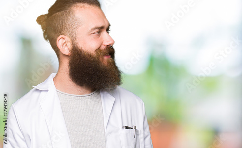 Young blond scientist man wearing white coat looking away to side with smile on face  natural expression. Laughing confident.
