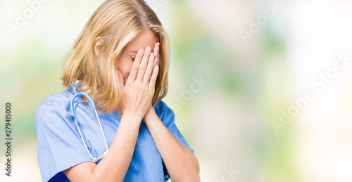 Beautiful young doctor woman wearing medical uniform over isolated background with sad expression covering face with hands while crying. Depression concept.