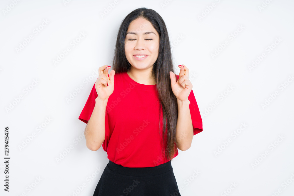 Beautiful brunette woman wearing red t-shirt over isolated background smiling crossing fingers with hope and eyes closed. Luck and superstitious concept. Beautiful brunette woman wearing red t-shirt over isolated background smiling crossing fingers with hope and eyes closed. Luck and superstitious concept.