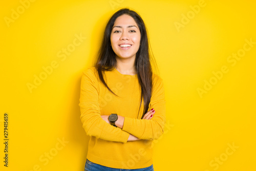 Beautiful brunette woman over yellow isolated background happy face smiling with crossed arms looking at the camera. Positive person. © Krakenimages.com