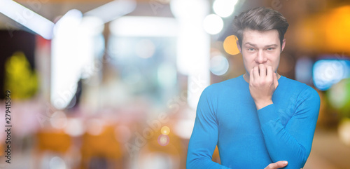 Young handsome man wearing blue sweater over isolated background looking stressed and nervous with hands on mouth biting nails. Anxiety problem. © Krakenimages.com
