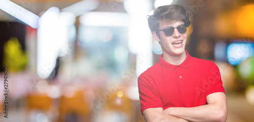 Young handsome man wearing sunglasses over isolated background happy face smiling with crossed arms looking at the camera. Positive person. © Krakenimages.com