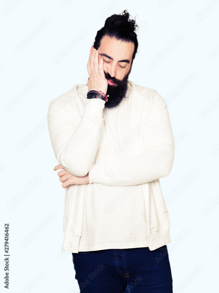 Young man with long hair and beard wearing sporty sweatshirt thinking looking tired and bored with depression problems with crossed arms. Young man with long hair and beard wearing sporty sweatshirt thinking looking tired and bored with depression problems with crossed arms.