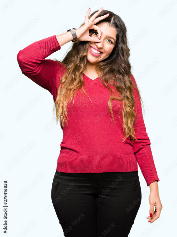 Young beautiful woman wearing red sweater doing ok gesture with hand smiling, eye looking through fingers with happy face. Young beautiful woman wearing red sweater doing ok gesture with hand smiling, eye looking through fingers with happy face.