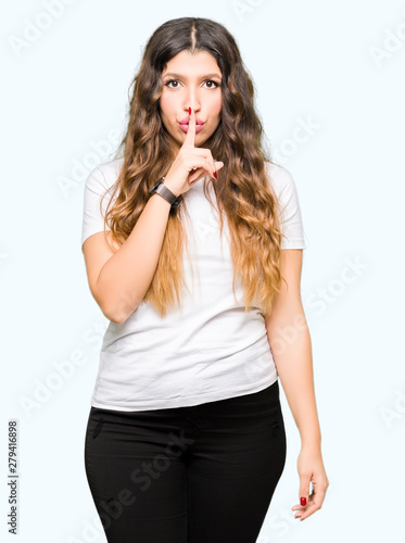 Young beautiful woman wearing casual white t-shirt asking to be quiet with finger on lips. Silence and secret concept.