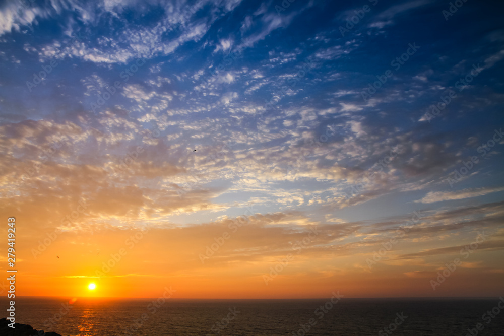Sunset above the sea landscape panorama with full yellow sun reflections over the Atlantic Ocean and beautiful blue sky with white clouds seen from Sagres, Portugal.