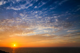 Sunset above the sea landscape panorama with full yellow sun reflections over the Atlantic Ocean and beautiful blue sky with white clouds seen from Sagres, Portugal.