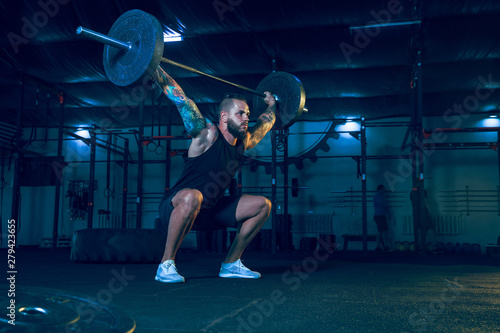 Young healthy man athlete doing exercise with the barbell in the gym. Single male model training hard and practicing in squats. Concept of healthy lifestyle  sport  fitness  bodybuilding  crossfit.