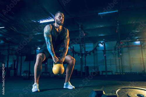 Young healthy man athlete doing exercise with the weights in the gym. Single male model training hard and practicing in squats. Concept of healthy lifestyle, sport, fitness, bodybuilding, crossfit.