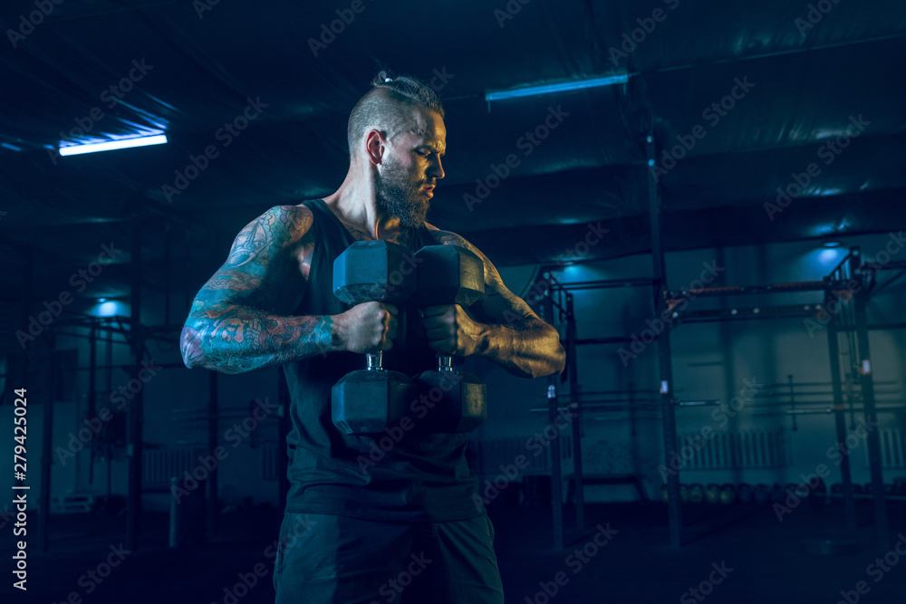 Naklejka premium Young healthy man athlete doing exercise with the weights in the gym. Single male model training hard his upper body, practicing. Concept of healthy lifestyle, sport, fitness, bodybuilding, crossfit.