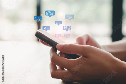 Social media interactions on mobile phone, concept with notification icons of like, message, email, comment and star above smartphone screen, person hands holding device, internet digital marketing