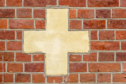 Red brick wall with white-yellowish cross sign background