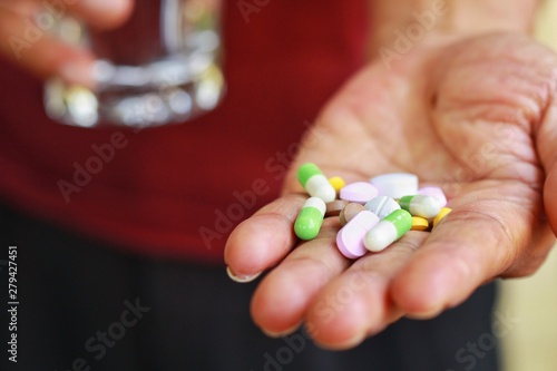 Elderly man holding pills(tablet and capsule) and glass of water in hands taking a lot of medicine, supplements or antibiotic antidepressant painkiller medication Hope for cure.Health concept. photo