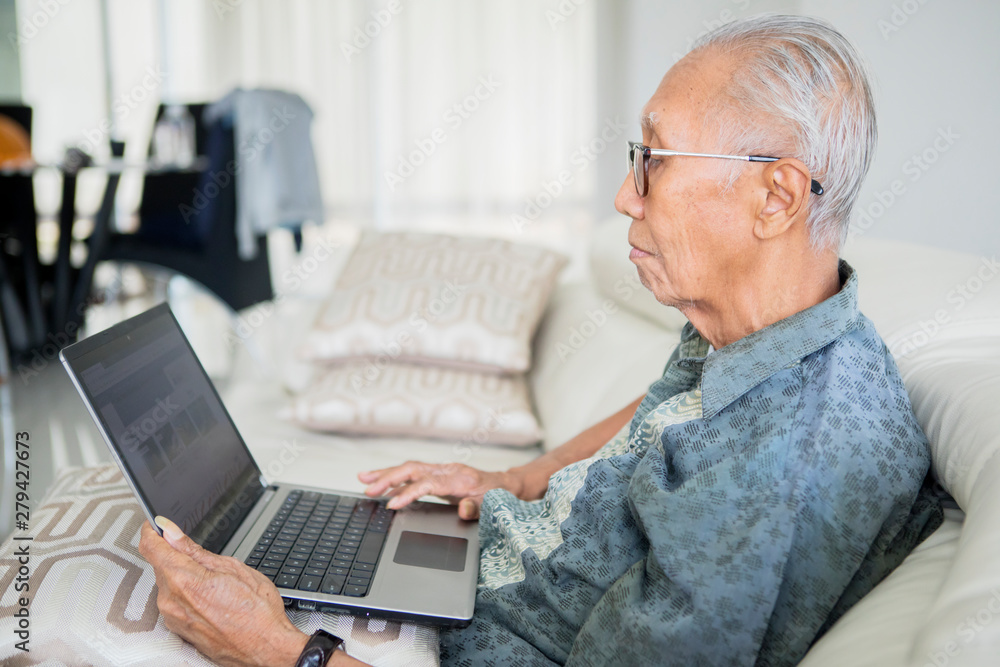 Old man using laptop computer on the sofa Old man using laptop computer on the sofa