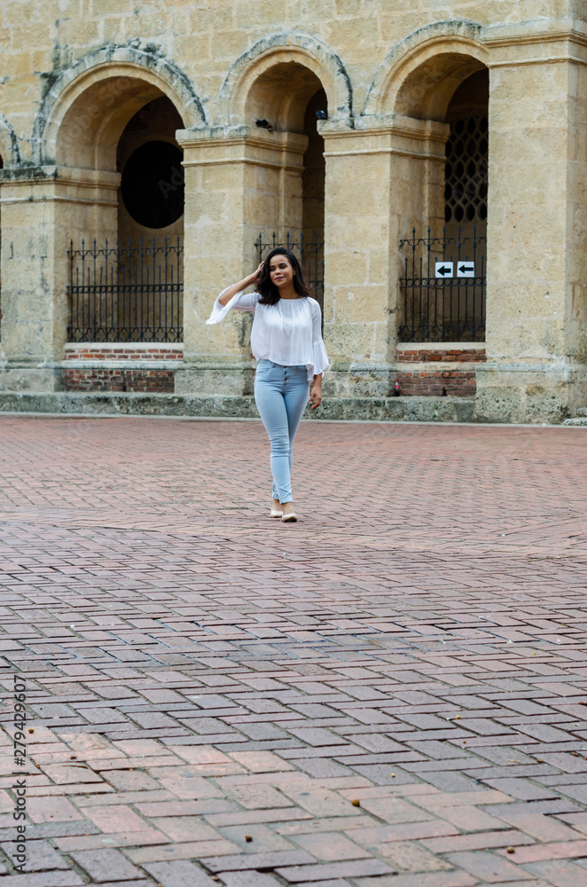 Outdoor portrait of young beautiful girl 9 to 25 years old posing in street. wearing white blouse and tight jeans and sapatillas. City lifestyle. Female fashion concept.