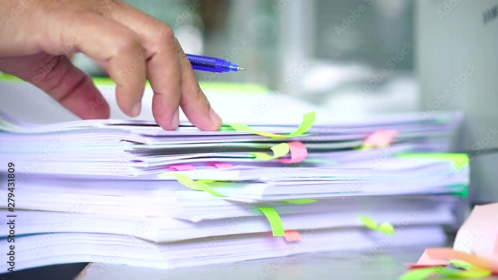Overwork of document report and business busy Concept: Businessman manager checking and signing documents reports papers on stacks of paper files with post-it on paperwork in overload at modern office