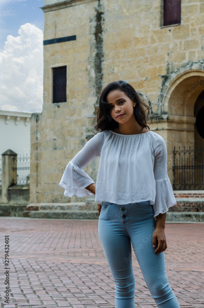 Outdoor portrait of young beautiful girl 9 to 25 years old posing in street. wearing white blouse and tight jeans and sapatillas. City lifestyle. Female fashion concept. Outdoor portrait of young beautiful girl 9 to 25 years old posing in street. wearing white blouse and tight jeans and sapatillas. City lifestyle. Female fashion concept.