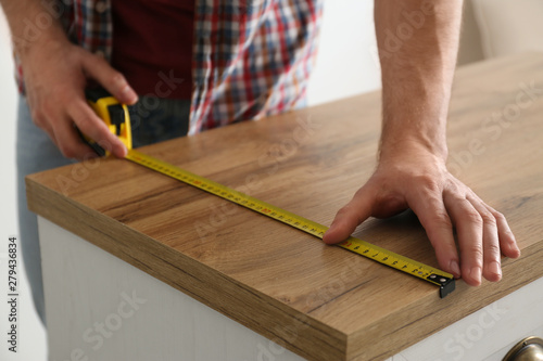 Man measuring wooden cabinet, closeup. Construction tool