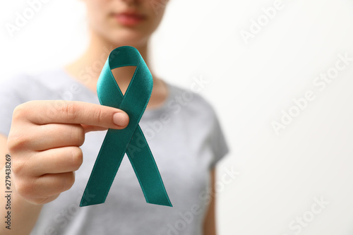 Woman holding teal awareness ribbon against light background, closeup