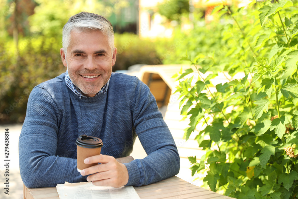 Handsome mature man sitting at table in park. Space for text Handsome mature man sitting at table in park. Space for text