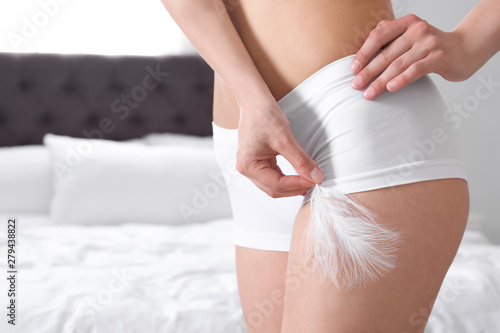 Closeup of woman touching leg with feather in bedroom, space for text. Epilation procedure