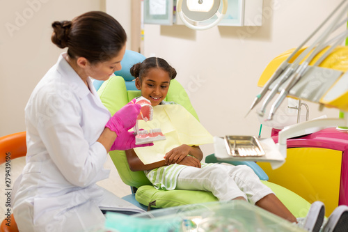 Dark-haired female doctor brushing an artificial teeth model