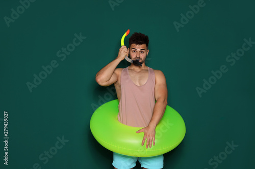 Funny young man with bright inflatable ring on dark green background © New Africa