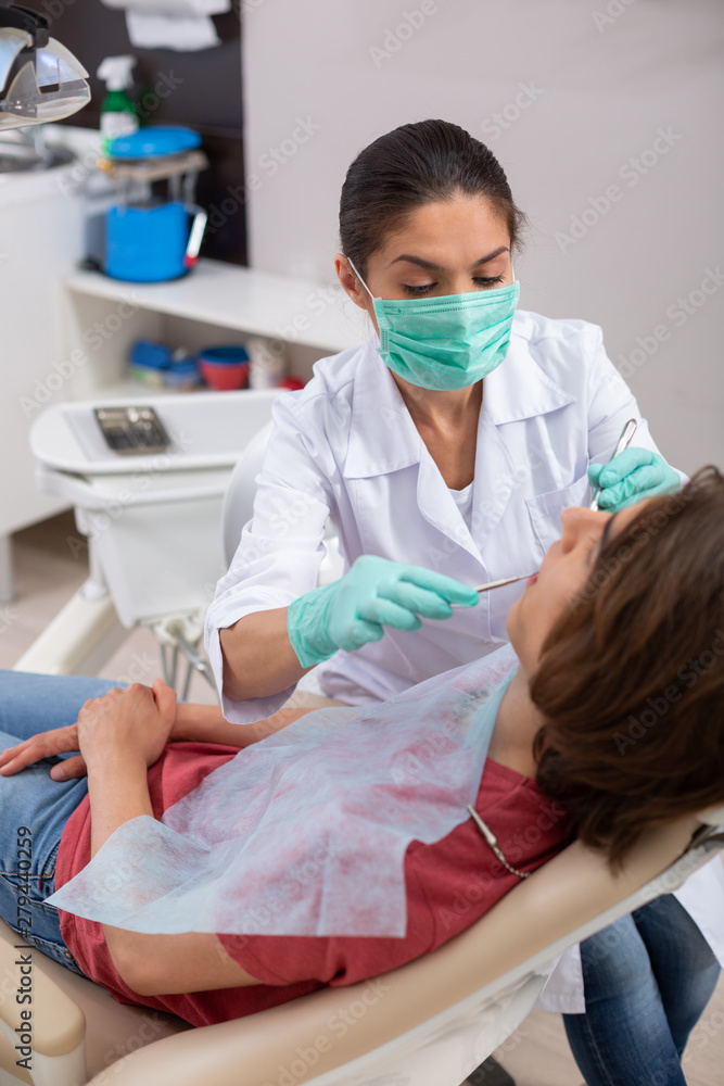 Concentrated dark-haired female dentist treating her patients teeth Concentrated dark-haired female dentist treating her patients teeth