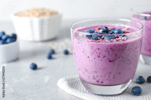 Glass of tasty blueberry smoothie with muesli on grey table. Space for text