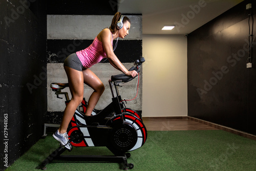 Woman exercise in gym on bike and liste music over headphones on her head