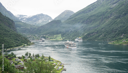 Panoramic view from the high mountains down to the Geiranger Fjord (UNESCO World Heritage Site). Three huge sea cruisers which look tiny like matchboxes  in the scenic bay. Green foliage framing. photo