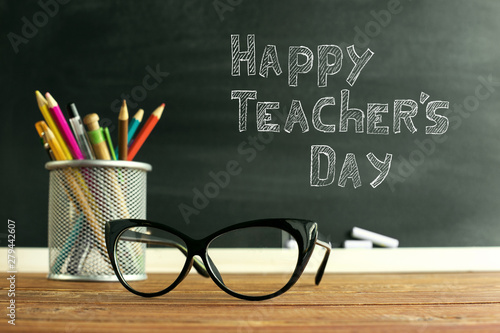 Glasses teacher and a stand with pencils on the table, on the background of a blackboard with chalk. The concept of the teacher's day. Copy space.