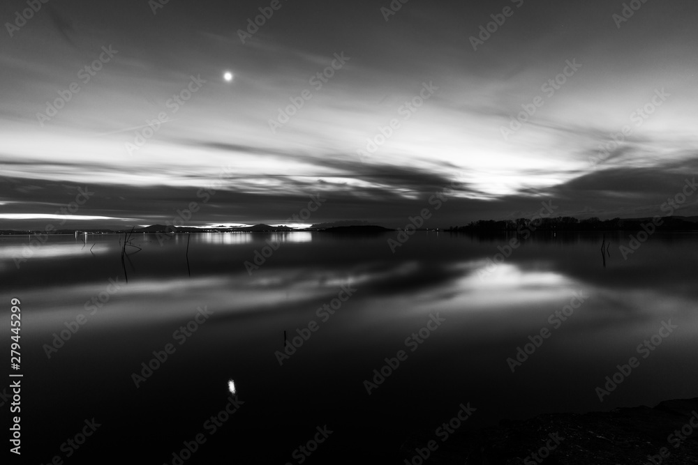 Moon above a lake with its reflection on the Trasimeno lake surface at dusk