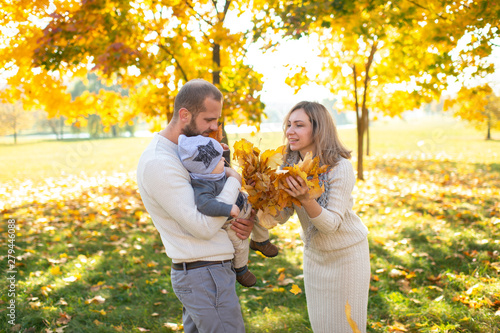 Beautiful family couple having fun with their child in autumn park.
