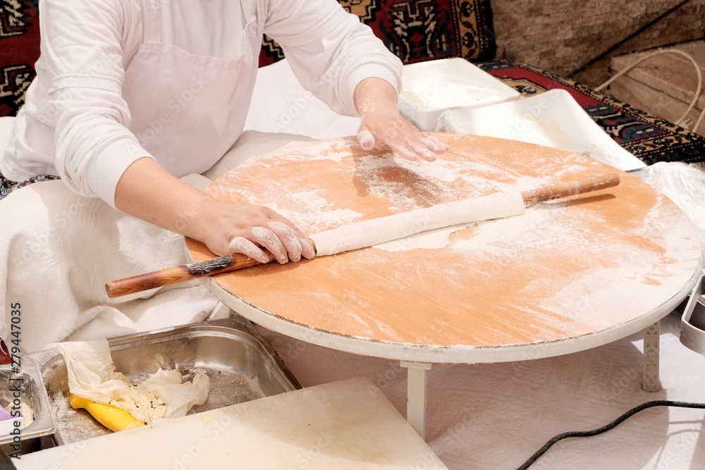 Eastern woman rolls out the dough with a rolling pin. A woman kneads, bakes cookies, pizza or bread. Turkish national dishes. Food is paid additionally according to the system 