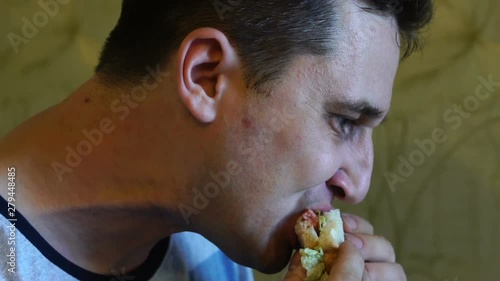 Cute young hungry caucasian man with an appetite is eating a tasty and juicy sandwich, carefully chewing up a close-up, slow motion
