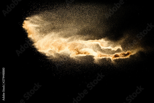 Abstract sand cloud.Golden colored sand splash agianst dark background.Yellow sand fly wave in the air. Sand explode on black background ,throwing freeze stop motion concept.