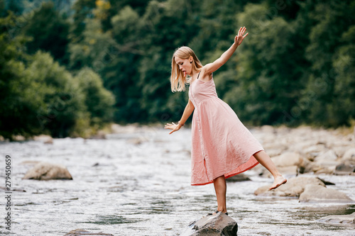 Young graceful ballerina girl balancing on stone in the river.