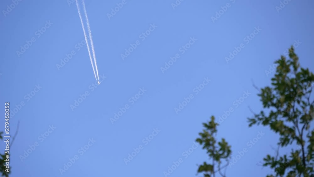 Jet airplane white trail above beautiful blue sky, in front of tree leaves slowly moving with the wind. Jet airplane white trail above beautiful blue sky, in front of tree leaves slowly moving with the wind.