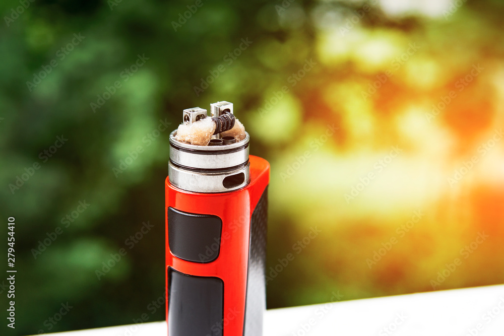 electronic cigarette on the background of trees, visible spiral wool and steam. Coil cleaning. electronic cigarette on the background of trees, visible spiral wool and steam. Coil cleaning.