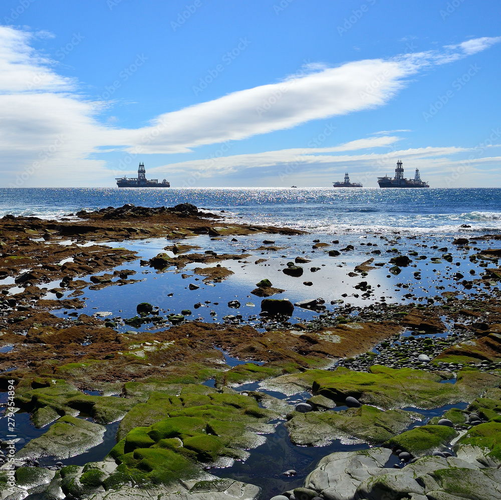 Colorful rocky beach at low tide in foreground and oil rigs in background       