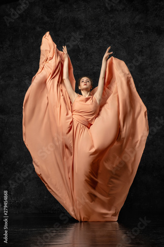 Ballerina. A young dancer dressed in a long peach dress picked up the edge of dress and raised up your hands in a butterfly pose. Performs a graceful, graceful dance movement. Beautiful classic ballet