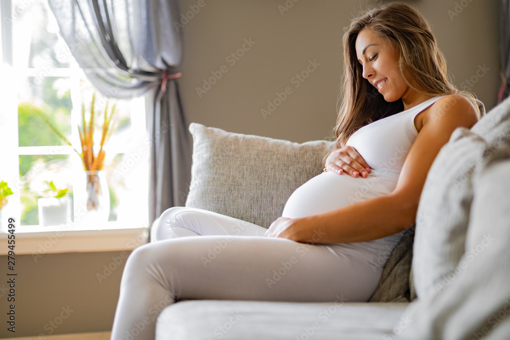 Smiling pregnant woman sitting in sofa looking at her stomach Smiling pregnant woman sitting in sofa looking at her stomach