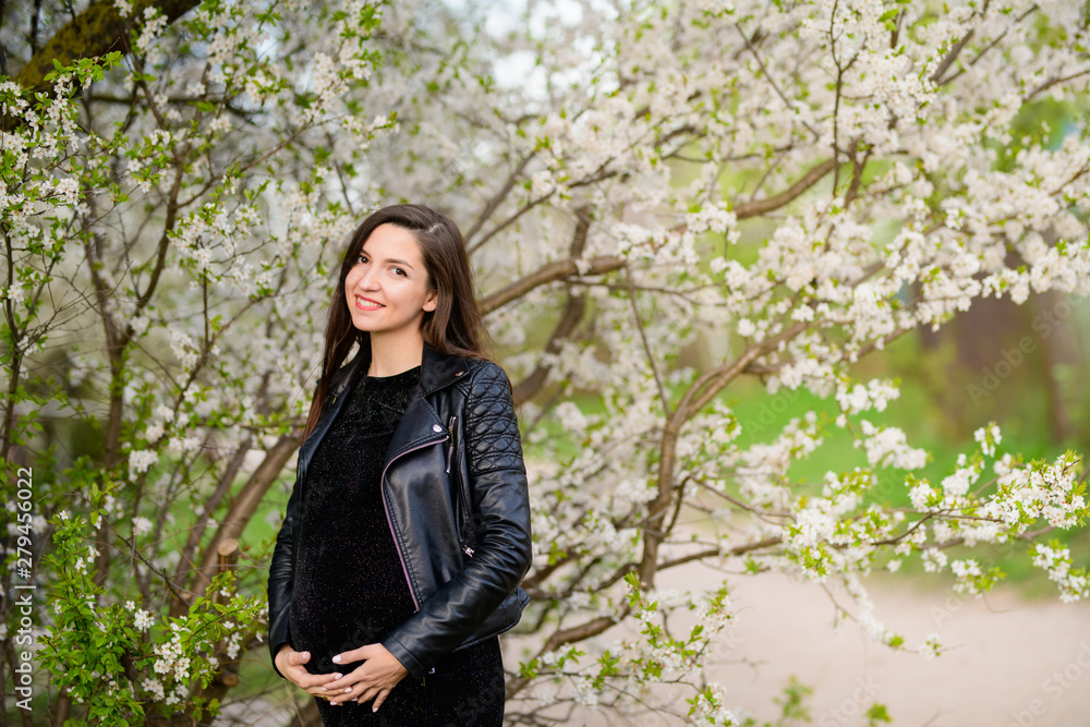 Pregnant girl in the flowered garden. beautiful pregnant girl in a black dress is standing in a flowered garden Pregnant girl in the flowered garden. beautiful pregnant girl in a black dress is standing in a flowered garden